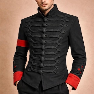 Può includere: Una giacca nera in stile militare con colletto alto, maniche lunghe con polsini rossi e una fascia rossa sul braccio destro. La parte anteriore è decorata con passanti in corda intrecciata nera e bottoni neri abbinati in modo simmetrico.