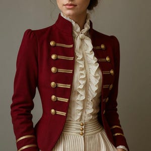 Può includere: Giacca bordeaux in stile militare con finiture e bottoni dorati. La giacca presenta un collo alto ed è abbinata a una camicetta color crema con volant e pantaloni a righe. Lo stile generale è vintage ed elegante.