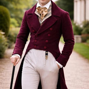 May include: A burgundy double-breasted frock coat with matching buttons, paired with light-colored trousers and a gold-toned ascot. The coat has a long tail and is worn with a white collared shirt. A black cane is held in the left hand.