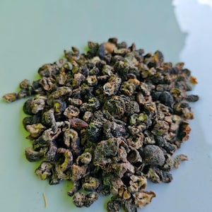 Puede incluir: Primer plano de un montón de hierbas secas, predominantemente de color marrón oscuro y verde. Las hierbas tienen una apariencia texturizada e irregular. La imagen se centra en los detalles del material vegetal seco.