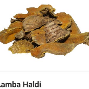 Puede incluir: Primer plano de Aamba Haldi, también conocido como jengibre de mango, sobre un fondo claro. Las piezas, marrones y amarillas, tienen una superficie texturizada. La imagen destaca la forma natural de esta especia.