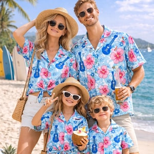 May include: A family of four wearing matching Hawaiian shirts with a blue floral and ukulele design. The shirts are light blue with pink flowers and blue ukuleles. They are on a sandy beach with surfboards and a tropical theme.