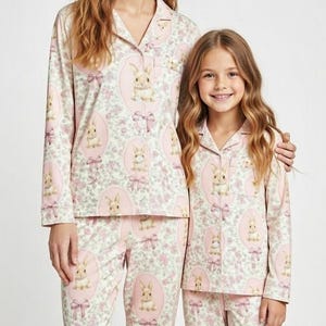 Puede incluir: Conjuntos de pijama rosas a juego con un motivo de conejito y lazo. Las camisetas y pantalones de manga larga presentan un dise&ntilde;o repetido de conejitos en marcos ovalados y lazos rosas. Los pijamas tienen un estilo cl&aacute;sico abotonado.