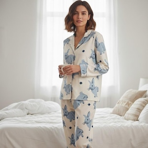 Op de afbeelding: Cr&egrave;mekleurige pyjamaset met een blauwe konijnenprint. De top met lange mouwen en de broek hebben een herhalend patroon van konijnen en sterren. De pyjama heeft een knoopsluiting en een relaxte pasvorm.