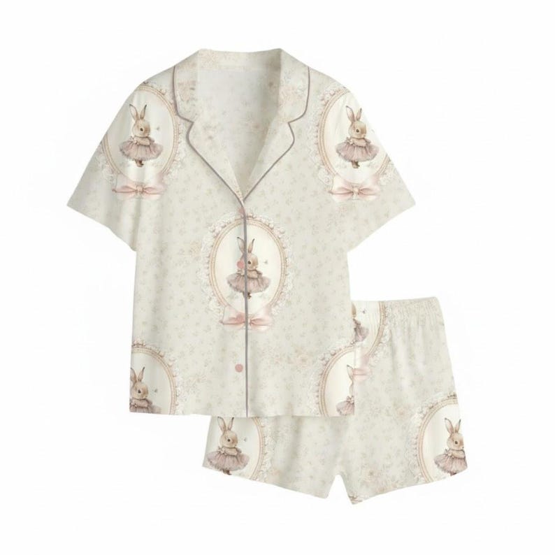 K&ouml;nnte beinhalten: Ein zweiteiliges hellbeige Pyjama-Set mit einem sich wiederholenden Muster eines H&auml;schens in einem Tutu in einem ovalen Rahmen. Das Set beinhaltet ein Hemd mit Kn&ouml;pfen und kurzen &Auml;rmeln sowie passende Shorts. Die Pyjamas haben rosa Akzente.