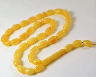 Op de afbeelding: Een streng amberkleurige gebedskralen met ovaalvormige kralen. De kralen zijn warmgeel van kleur, sommige vertonen kleurvariaties. De kralen zijn geregen met een bijpassend geel koord.