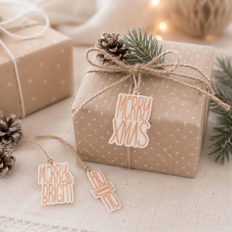 Drei Geschenkanhänger Weihnachten in Creme und Kupfer an und neben einem natürlich verpackten Weihnachtsgeschenk mit Tannenzweig und Zapfen.