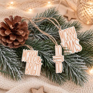 Drei Anhänger für Weihnachtsgeschenke mit Merry Xmas, Merry & Bright und Ho Ho Ho auf winterlichem Tannengrün als festliche Geschenkdekoration.
