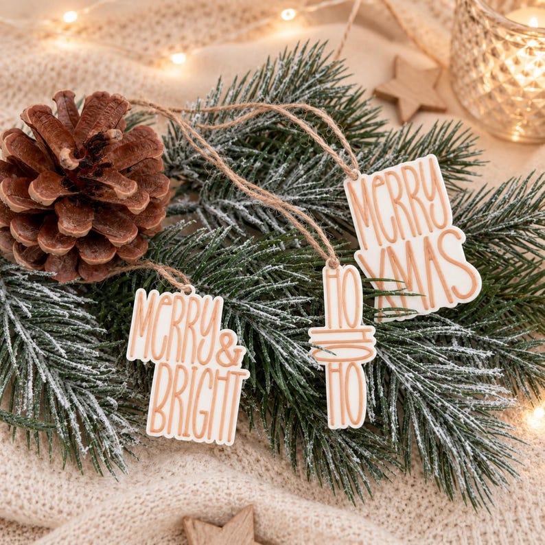 Drei Anhänger für Weihnachtsgeschenke mit Merry Xmas, Merry & Bright und Ho Ho Ho auf winterlichem Tannengrün als festliche Geschenkdekoration.