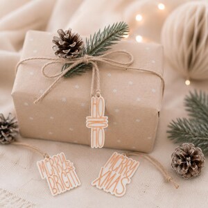 Ho Ho Ho Anhänger an einem schlicht verpackten Weihnachtsgeschenk, daneben Merry Xmas und Merry & Bright als Idee zum originell Verpacken.