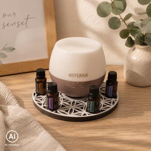 Könnte beinhalten: Ein weiß-brauner dōTERRA Diffusor für ätherische Öle mit abgerundeter Form, platziert auf einem runden Untersetzer mit weiß-schwarzem geometrischem Muster, umgeben von vier kleinen bernsteinfarbenen Glasfläschchen mit schwarzen Deckeln.