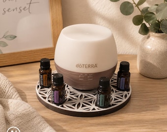 May include: A white and brown dōTERRA essential oil diffuser with a rounded shape, positioned on a circular white and black geometric patterned coaster, surrounded by four small amber glass essential oil bottles with black caps.