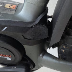 Könnte beinhalten: Nahaufnahme eines Teils eines Fahrradrahmens mit einem Bosch Performance Line CX Motor. Der Rahmen ist grau und der Motor ist schwarz. Ein schwarzes Gummipolster ist in der Nähe des Motors zu sehen.