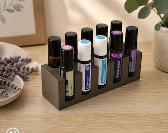 Könnte beinhalten: Ein rechteckiger, dunkelgrauer Betonständer mit acht ätherischen Öl-Roll-on-Flaschen. Die Flaschen haben schwarze Kappen und Etiketten mit Texten wie dōTERRA, Gardenia, Calmer, Rescuer, PastTense und Lavender, angeordnet in zwei Reihen.