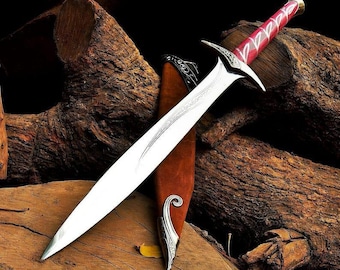 May include: A silver sword with a red handle and a brown sheath rests on a pile of wood. The sword has a long, sharp blade and a decorative hilt. The sheath is made of brown leather and has silver accents.
