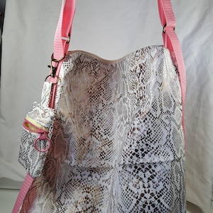 Op de afbeelding: Een grote tote bag met een slangenprint in wit, goud en zwart. Het heeft een bijpassend klein zakje en roze bandjes. De tas heeft een schouderriem en een kleinere riem voor het zakje.