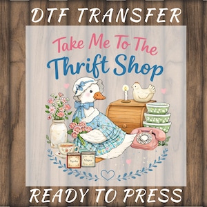 May include: DTF transfer with the text "Take Me To The Thrift Shop" and "Ready To Press". The design features a cartoon duck in a blue dress, surrounded by vintage items like a phone, bowls, and spices.
