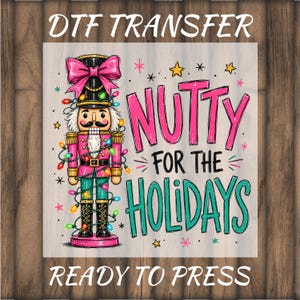 May include: A DTF transfer design featuring a nutcracker wearing a large pink bow, decorated with colorful string lights. The text reads DTF TRANSFER, NUTTY FOR THE HOLIDAYS, and READY TO PRESS. The illustration includes small yellow stars and pink accents.