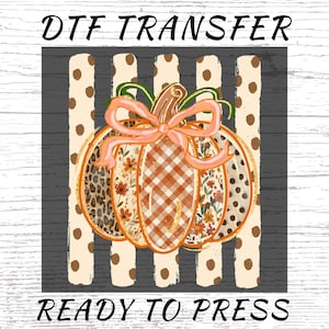 May include: A DTF transfer ready to press featuring a central pumpkin graphic with a peach-colored bow. The pumpkin has segments with leopard print, orange plaid, and floral patterns. It sits against a background of vertical beige stripes with brown dots.