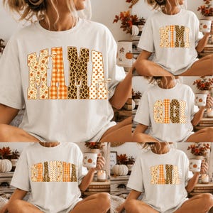 May include: A white short-sleeved t-shirt featuring large block letters with varied autumn-themed patterns including orange plaid, leopard print, and floral designs. The text options displayed across different shirts include MAMA, MIMI, GIGI, GRANDMA, and NANA.