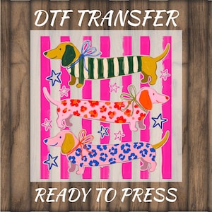 May include: A DTF transfer ready to press featuring three dachshunds on a pink and white striped background with blue stars. The top dog is yellow with green stripes, the middle is pink with red flowers, and the bottom is pink with blue spots.