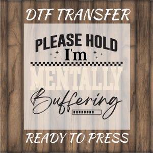 May include: DTF transfer with the text "PLEASE HOLD I'm MENTALLY Buffering READY TO PRESS" in black and light beige. The design includes stars, a checkered pattern, and a loading bar. The background is a light wood grain.