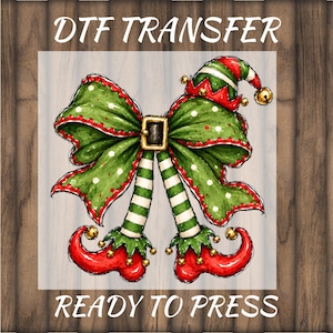 May include: A DTF transfer ready to press featuring a green and red elf-themed bow with white polka dots, a black belt buckle, and two striped legs ending in curled red elf shoes with small gold bells attached to the tips and edges.