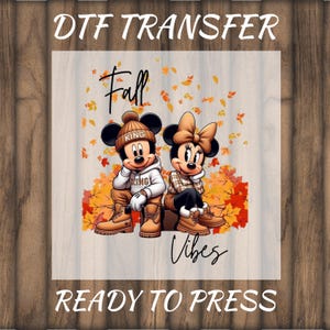 May include: DTF transfer featuring Mickey and Minnie Mouse in fall attire, with the words "Fall Vibes." Mickey wears a beanie and hoodie, while Minnie has a bow. The words "DTF TRANSFER" and "READY TO PRESS" are at the top and bottom.