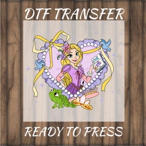 May include: DTF transfer featuring a cartoon illustration of a princess with long blonde hair, wearing a purple dress, and holding a book. The design includes a frog, a crown, and the text "READY TO PRESS". The background is a heart-shaped frame.