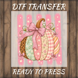 May include: A DTF transfer ready to press featuring a pumpkin with vertical segments in various patterns including leopard print, floral, stars, and gingham. The pumpkin is decorated with a large glittery pink bow and smaller bows, set against a pink striped background.