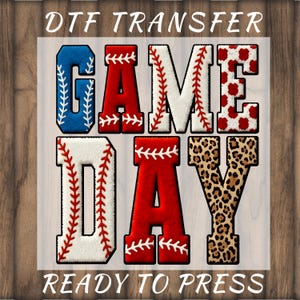 May include: DTF transfer featuring the words "GAME DAY" in a baseball design. The letters are in blue, red, white, and leopard print. The text "READY TO PRESS" is also included. The design is suitable for pressing onto fabric.