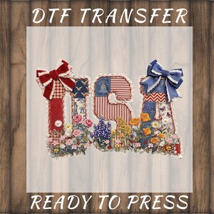 May include: DTF transfer design featuring the letters "USA" decorated with patriotic patterns, floral accents, and bows. The letters are filled with red, white, and blue fabrics and surrounded by a variety of flowers. The text "READY TO PRESS" is also included.