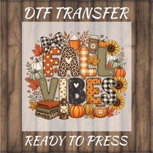 May include: A DTF transfer featuring the text FALL VIBES in patterned block letters surrounded by autumn elements including pumpkins, sunflowers, maple leaves, a plaid bow, a lantern, a coffee cup, and folded blankets on a wood background.