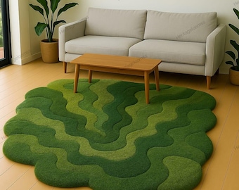 Op de afbeelding: Een groene vloerkleed met een golvend patroon en verschillende groentinten. Een houten salontafel staat op het kleed voor een lichtgrijze bank. Potplanten op de achtergrond voegen een natuurlijk element toe aan de kamer. Afmetingen: ongeveer 200 cm x 150 cm.