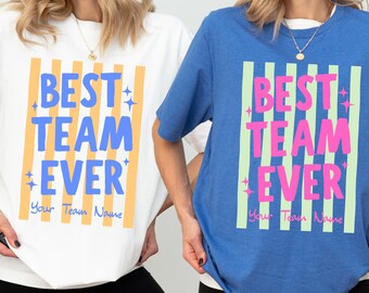Może przedstawiać: Biały t-shirt z niebieskim napisem BEST TEAM EVER oraz Your Team Name na żółtych paskach oraz niebieski t-shirt z różowym napisem BEST TEAM EVER oraz Your Team Name na jasnych zielonych paskach, oba ozdobione małymi akcentami w kształcie gwiazdek.