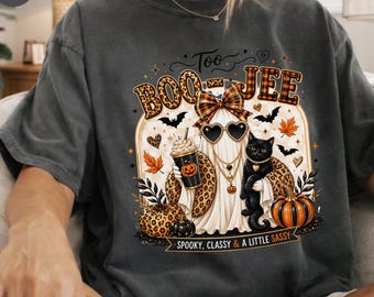 Może przedstawiać: Ciemnoszary t-shirt z grafiką ducha w kraciastej kokardzie i okularach przeciwsłonecznych w kształcie serc, trzymającego kubek kawy. Wzór zawiera czarnego kota, dynie, nietoperze oraz napis "Too BOO-JEE" i "SPOOKY, CLASSY & A LITTLE SASSY."
