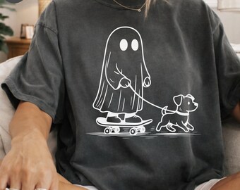 Może przedstawiać: Ciemnoszary t-shirt z krótkim rękawem z białym nadrukiem graficznym przedstawiającym ducha stojącego na deskorolce i trzymającego smycz przyczepioną do małego psa. Koszulka ma okrągły dekolt i tkaninę o wyblakłej, vintage fakturze.
