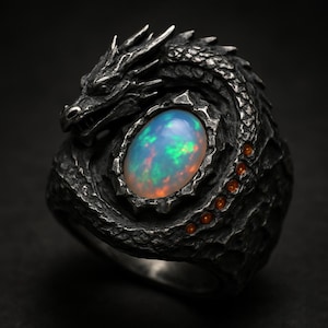 May include: A detailed, silver-toned ring featuring a dragon design. The dragon wraps around a large, oval opal gemstone with blue, green, and orange hues. Small orange gemstones accent the dragon's body. The ring has a textured, antique finish.
