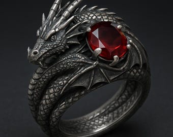 Può includere: Un anello a forma di drago color argento con una grande gemma rossa ovale. La testa e il corpo del drago avvolgono l'anello, con squame e ali dettagliate. La gemma è incastonata negli artigli del drago.