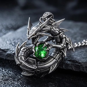 May include: A silver-colored dragon pendant necklace with a large, faceted green gemstone clutched in its claws. The dragon has intricate details and is set against a dark, textured background. The necklace chain is also silver.