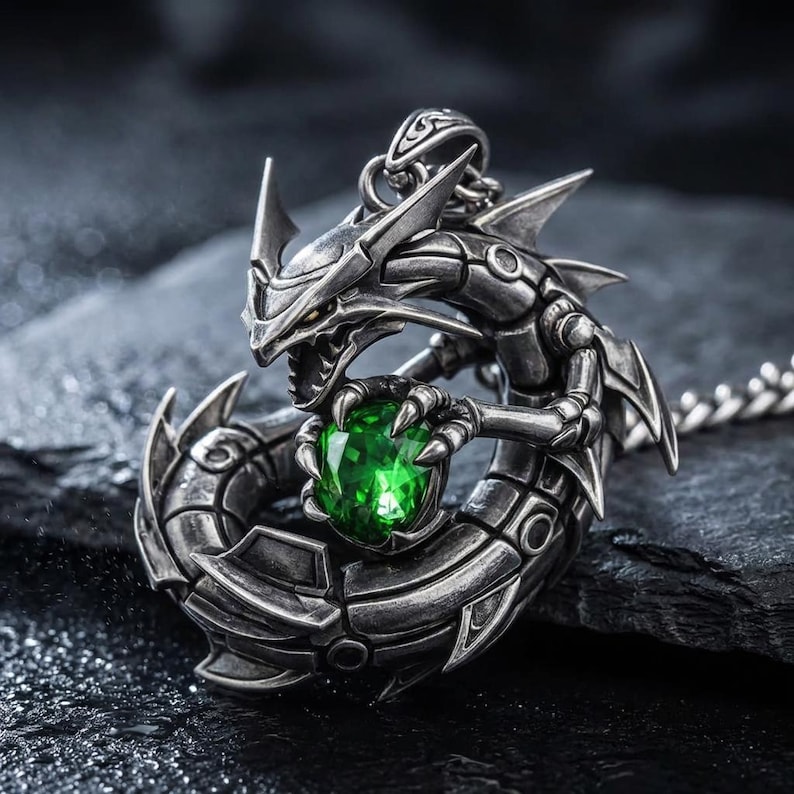May include: A silver-colored dragon pendant necklace with a large, faceted green gemstone clutched in its claws. The dragon has intricate details and is set against a dark, textured background. The necklace chain is also silver.