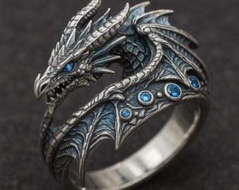 May include: A silver dragon ring with intricate detailing. The dragon's head features blue eyes and is surrounded by textured wings. The ring is accented with blue gemstones, creating a fantasy-themed accessory.
