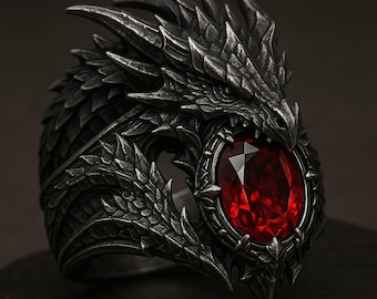 May include: A detailed, dark silver dragon ring with a large, oval, red gemstone. The dragon's head forms the ring's top, with intricate scales and sharp details. The gemstone is set in a decorative bezel.