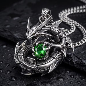 May include: A silver-colored dragon pendant necklace. The dragon is intricately detailed, holding a large, round, green gemstone. The necklace chain is also silver. The pendant is on a dark, textured surface.