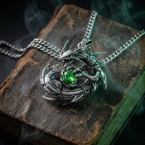 May include: A silver dragon pendant necklace with a green gemstone clutched in its claws. The dragon is detailed with intricate scales and a menacing expression. The necklace rests on a worn, leather-bound book.