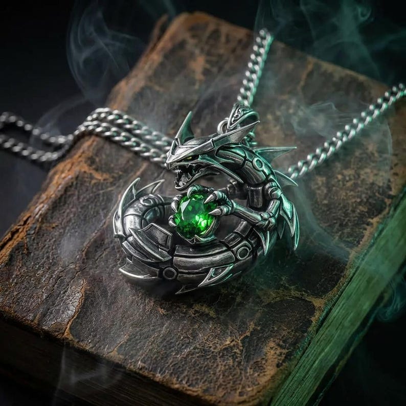 May include: A silver dragon pendant necklace with a green gemstone clutched in its claws. The dragon is detailed with intricate scales and a menacing expression. The necklace rests on a worn, leather-bound book.