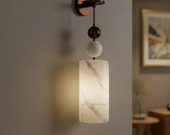 May include: A modern wall sconce with a cylindrical, marble-patterned shade. The fixture features a bronze-colored mounting plate and decorative elements, including a sphere and a marble ball. The light fixture is mounted on a gray wall.