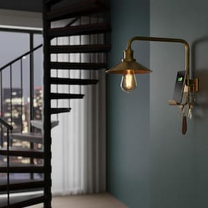 Puede incluir: Una lámpara de pared de latón antiguo con una bombilla Edison vintage, una estación de carga para teléfono y un llavero. La lámpara está montada en una pared verde azulado, con una escalera de caracol y luces de la ciudad en el fondo.