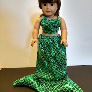 Puede incluir: Un disfraz de cola de sirena verde para una mu&ntilde;eca. La cola est&aacute; hecha de tela brillante con un patr&oacute;n de escamas. El disfraz incluye una parte superior a juego.