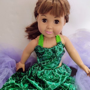 Puede incluir: Una mu&ntilde;eca con un disfraz de sirena verde y una falda de tul morado. La mu&ntilde;eca tiene el pelo casta&ntilde;o y los ojos marrones.